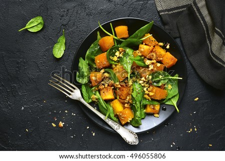 Roasted pumpkin salad with spinach and walnut on a black plate on a stone background.Top view.