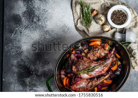 Roasted rabbit legs in pan with bulb of garlic and rosemary. Top view. Organic meat. Space for text