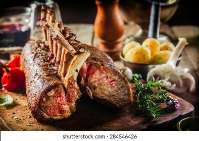 Roasted Rectangle Rack of Lamb Chops on Wooden Cutting Board Surrounded by Herbs and Fresh Ingredients