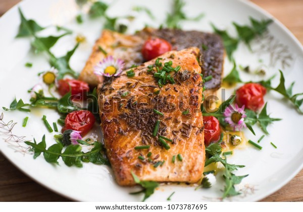 Roasted red salmon\
trout (steelhead) with tomato and decorative dandelion leaf and\
edible daisy flower on\
plate.