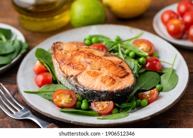 Roasted salmon steak with baby spinach and cherry tomatoes on a plate. Healthy meal