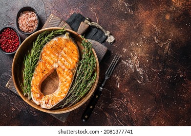 Roasted Salmon Trout Fish Steak in a vintage wooden plate with thyme and rosemary. Dark background. Top view. Copy space