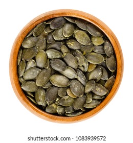 Roasted And Salted Pepita Pumpkin Seeds In Wooden Bowl, Used As Snack. Flat Green Edible Summer Squash Seeds Of Cucurbita Pepo. Isolated Macro Food Photo Close Up From Above On White Background.