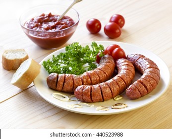 Roasted sausage with bread, herbs, sauce and tomatoes served on white plate and wood board