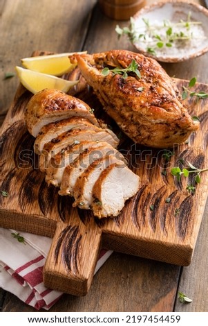 Roasted or seared chicken breast sliced on a cutting board with herbs and spices