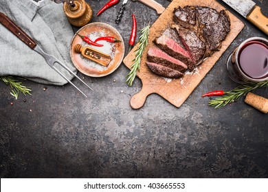 Roasted Sliced Grill Steak On Wooden Cutting Board With Wine, Seasoning And Meat Fork On Dark Vintage Metal Background, Top View, Border