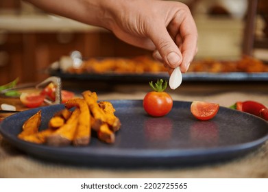 Roasted Sweet Potatoes. Baked Dish With Organic Batata With Cherry Tomatoes And Rosemary Herbs. Banner. Menu, Recipe. Close-up Chef's Hand Putting A Garlic Clove On A Plate With Fried Sweet Potatoes