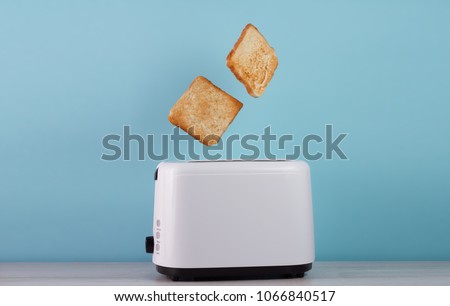 Roasted toast bread popping up of stainless steel toaster on a blue backgroun.Space for text