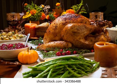 Roasted turkey garnished with cranberries on a rustic style table decoraded with pumpkins, gourds, asparagus, brussel sprouts, baked vegetables, pie, flowers, and candles.