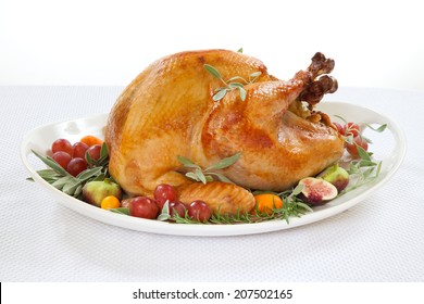 Roasted turkey on tray garnished with red grapes, figs, kumquat, and herbs over white background 