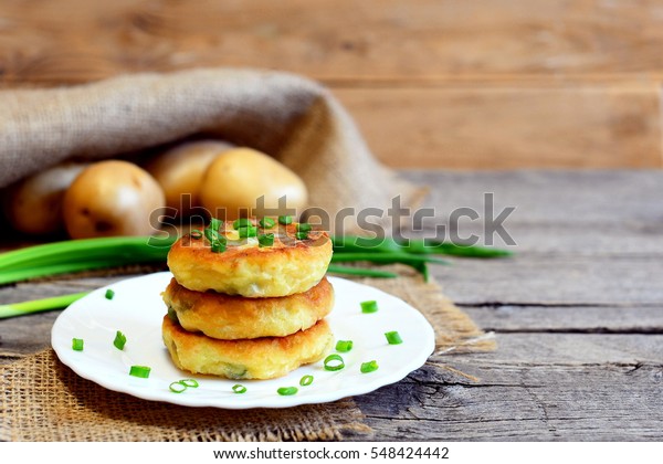 Roasted vegetable\
patties. Potato patties with vegetables and spices on plate and on\
wooden table. Raw potatoes, fresh green onions. Rustic style.\
Closeup. Tasty vegetarian\
recipe