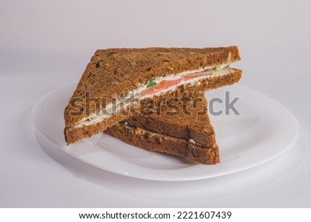 Roasted white bread and salmon. Triangular toast with fish, tomato and salad. Food concept, sandwich on a white plate and black background