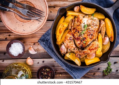 Roasted whole chicken with potatoes and thyme in a cast iron skillet