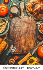 Roasted Whole Chicken Or Turkey, Pumpkins, Corn And Harvest Vegetables With Kitchen Knife And Cutlery Served Around Aged Wooden Cutting Board On Dark Rustic Background, Frame. Thanksgiving Day Food