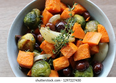 Roasted Winter Vegetables With Chestnuts And A Sprig Of Thyme Inside A Ceramic Bowl On A Wooden Background, Top View