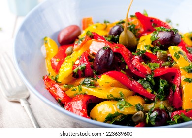 Roasted Yellow And Red Bell Pepper Salad With Capers And Olives In A Blue Bowl On A White Background. Grilled Vegetables.