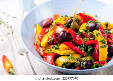 Roasted yellow and red bell pepper salad with capers and olives in a blue bowl on a white background. Grilled vegetables. - Powered by Shutterstock