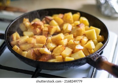 Roasting Fresh Potatoes In A Cast Iron Skillet With Sunflower Oil. A View Of A Stovetop With A Frying Pan Filled With Golden Fried Potatoes In A Real Kitchen. Food Cooked In A Homemade Frying Pan