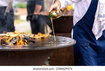 Roasting meat on a round barbecue with an open fire. The cook pours oil on the brazier - Powered by Shutterstock