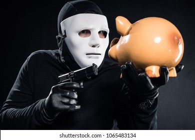 Robber In Balaclava And Mask Aiming At Piggy Bank