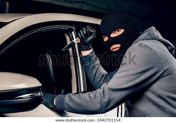 The robber in\
Balaclava threatening with a knife takes away a bag from the driver\
of a car. The concept of\
crime