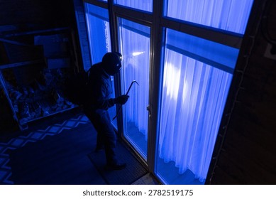 Robber in black clothes using crowbar to open balcony door to enter the house at night, above outdoors view