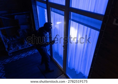 Robber in black clothes using crowbar to open balcony door to enter the house at night, above outdoors view