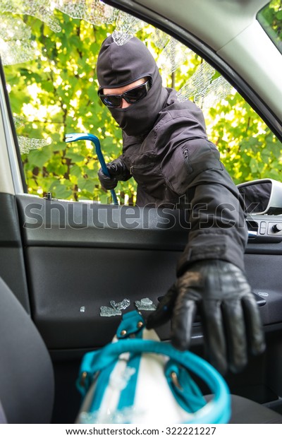 Robber\
breaking a car\'s windows to steal a woman\
bag.