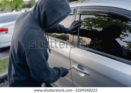 Robber breaking into a car at the parking lot.
