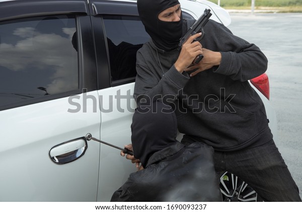 A robber dressed in black holding crowbar\
at a driver in a car. Car thief\
concept.
