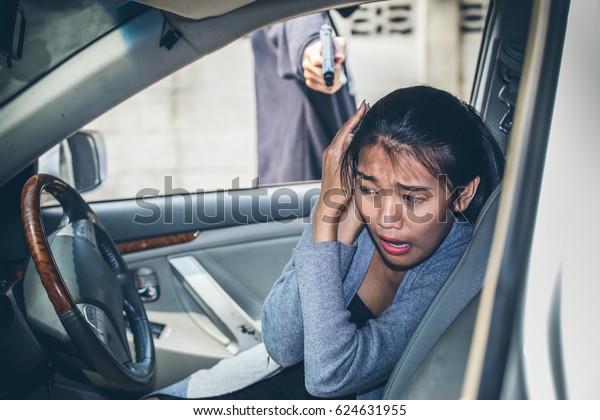 A robber dressed in black pointing a
gun at a women driver in a car. Car thief
concept.