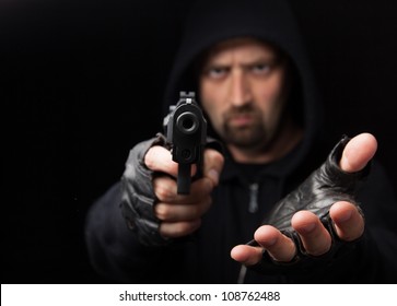 Robber With Gun Holding Out Hand Against A Black Background