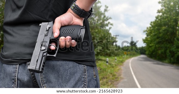 Robber\
holds 9mm automatic pistol gun in right hand and stands beside the\
road in countryside to robber the  passengers and drivers who\
passing this road, robbery on the road\
concept.