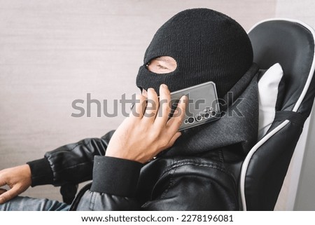 Robber making phone gesture. The concept of telephone terrorism and fraud. A masked man makes a phone call.
