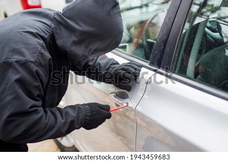 Robber man in black hoodie jacket using a screwdriver  to break lock and steal a vehicle. Car thief or theft for insurance concept.