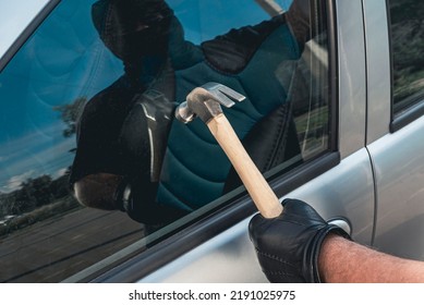 Robber Man In Mask With A Hammer Breaks The Car Door Window. The Concept Of Robbery Or Auto Theft.