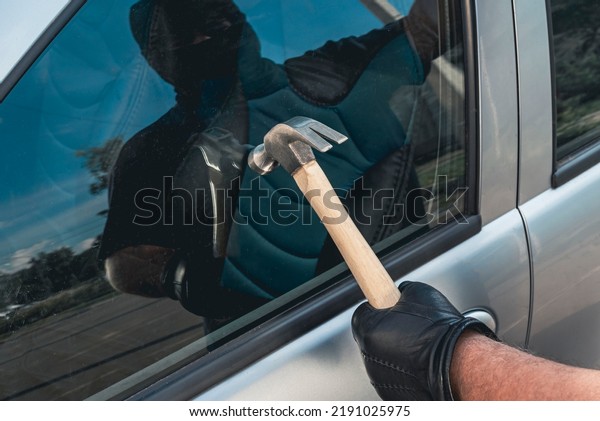 Robber man in mask with a\
hammer breaks the car door window. The concept of robbery or auto\
theft.