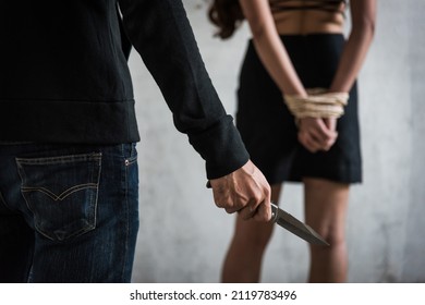 Robber man using knife to intimidate young woman take off her shirt sexual raping rope tied arm standing facing wall, criminal concept