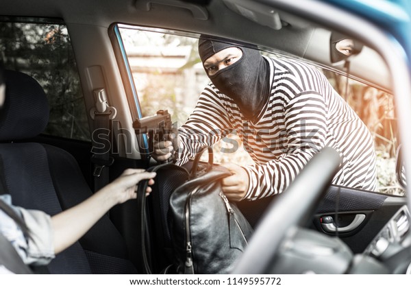 Robber pointing a gun to scare\
young woman and try to rob her car.andit man with masked robber\
holding handgun weapon gangster to hijack hostage woman driver car\
.