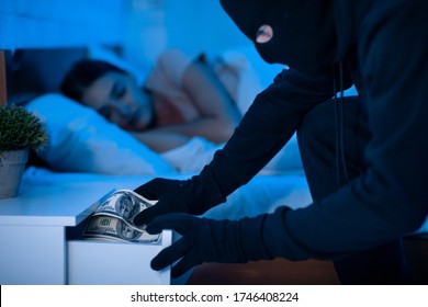 Robber stealing money from drawer in the night, breaking in house with peaceful female tenant sleeping in the background