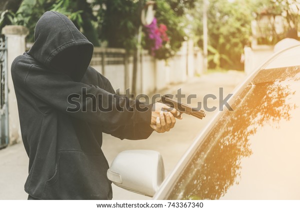 Robber or terrorist pointed his gun at\
the passenger or driver in a car on roadside background. Bad man\
Kill victim in Car. money,people and crime concept.\
