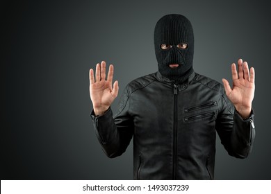 Robber, a thug in a balaclava raised his hands on a black background, surrenders. Robbery, hacker, crime, theft, arrest. Copy space