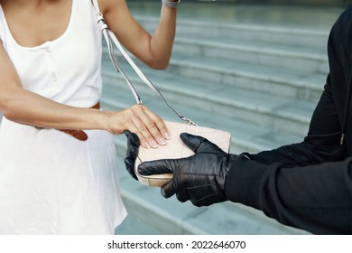 Robber Want To Steal Handbag Of Girl. Partial Image Of Bandit Wear Black Hoodie And Gloves. Woman Wear White Dress. Concept Of Robbery. City Daytime