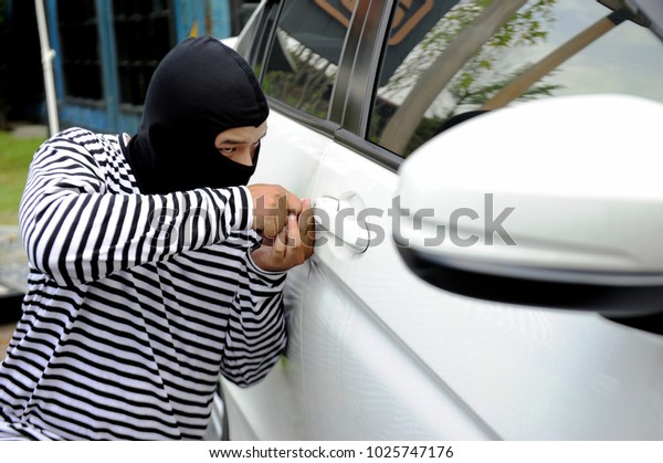 Robber wearing black and white striped shirt trying\
to open white car door