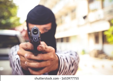Robber lleva un pantalones rayado en blanco y negro, lleva una máscara, cubre su cara, sostiene una pistola para robar la propiedad. Conceptos de seguridad en la vida y la pobreza