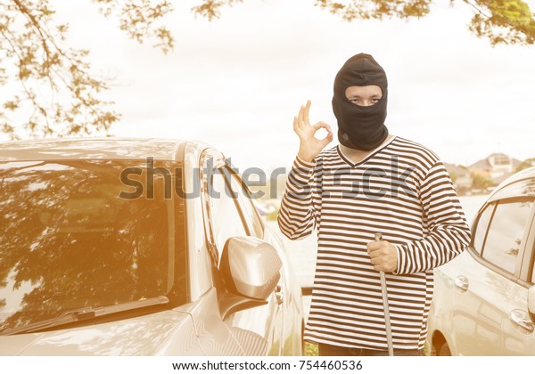 The robbers wearing a balaclava ready to\
burglary against car background. Select focus and use effect\
filter. Insurance crime Threat unemployed, Economic problems,\
cover-19 virus Concept.