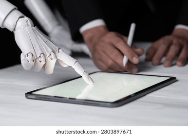 Robot hand and human hand working together on a digital tablet.