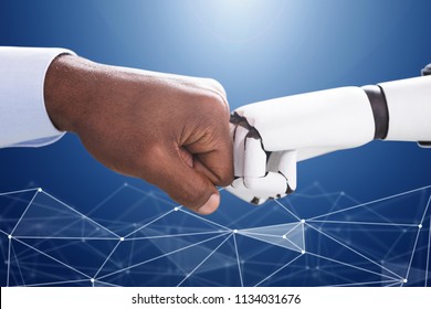 Robot And Human Hand Making Fist Bump On Blue Digital Backdrop