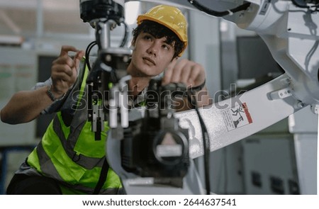 Robot maintenance engineer working on robot arm connection. Young adult man learning training robotic machine engineering in futuristic electronic education academy. Artificial intelligence technician