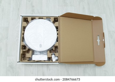 Robot Vacuum Cleaner In A Cardboard Box On A White Wooden Floor. View From Above.